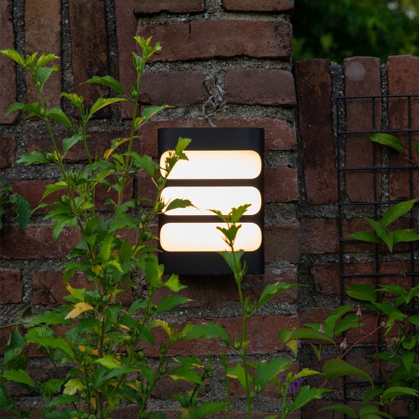 Schwarze LED-Außenwandleuchte mit drei horizontalen Lichtauslässen, montiert an einer Ziegelwand im Garten.