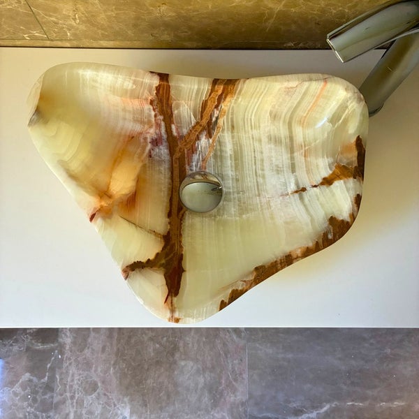 Asymmetrisches Aufsatzwaschbecken aus Naturstein mit brauner Maserung auf einer weißen Arbeitsplatte.