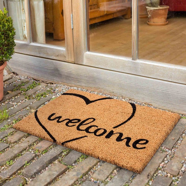 Fußmatte aus Kokosfaser mit Herz und Willkommensaufschrift vor einer Tür