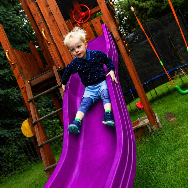 Heller Garten mit einem Spielturm aus Holz, einer lila Wellenrutsche und einem Kind.