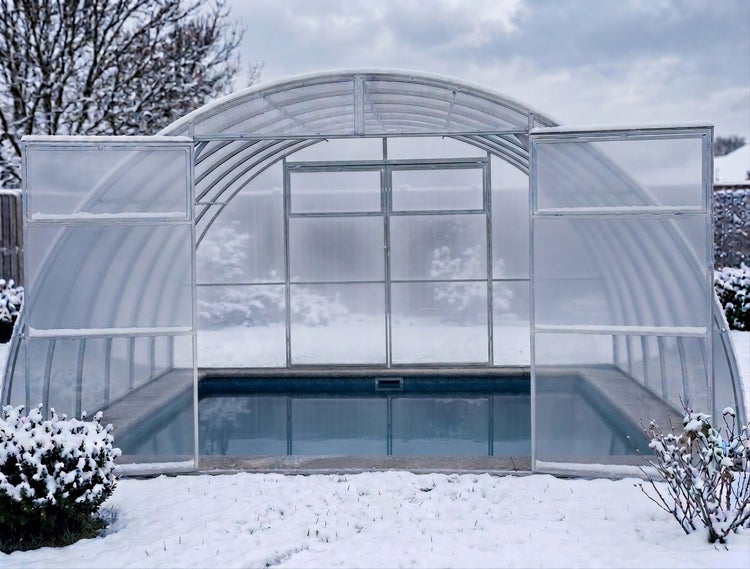 Begehbare Poolüberdachung aus Aluminium und Polycarbonat mit gewölbtem Dach im verschneiten Garten.