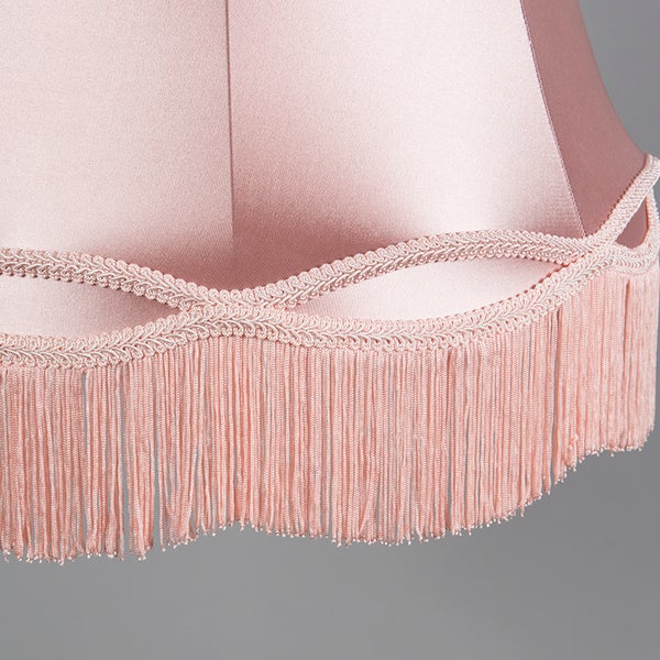 Detailaufnahme eines Lampenschirms aus Textil mit dekorativer Borte und Fransenabschluss.