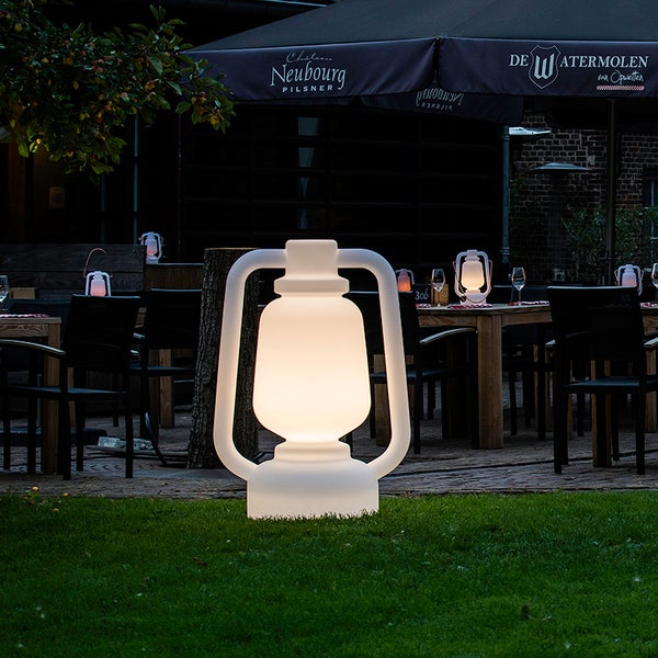 Große, leuchtende Outdoor Laterne als Dekoration für den Garten auf einer Rasenfläche vor einer Restaurantterrasse bei Dämmerung.