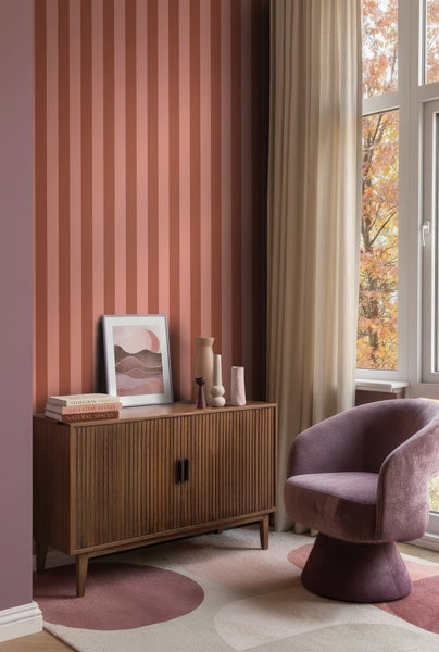 Gestreifte Tapete in Terrakotta und Mauve in einem Wohnzimmer mit Holz-Sideboard, Polstersessel und gemustertem Teppich.