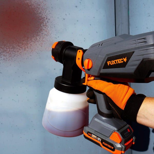 Handwerker mit Fuxtec Akku-Farbsprühsystem beim Auftragen von roter Farbe auf eine Wand.