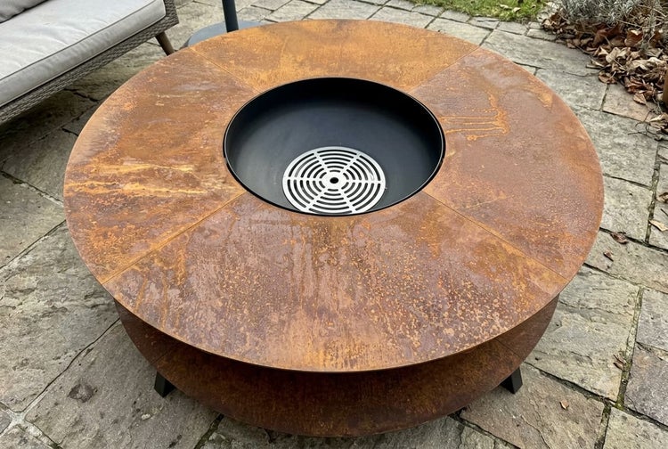 Runde Feuerschale mit Grillplatte aus Metall in Rostoptik und integriertem Grillrost auf einer Steinterrasse