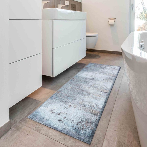 Ein rechteckiger Badläufer mit strukturiertem Muster liegt auf einem Fliesenboden in einem modernen Badezimmer mit Badewanne und Waschbecken.