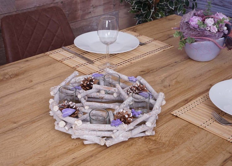 Tischdekoration mit Holzkranz, Teelichthaltern und Tannenzapfen auf einem Holztisch