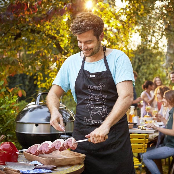 Mann würzt Fleischspieße am Grillplatz mit Gästen