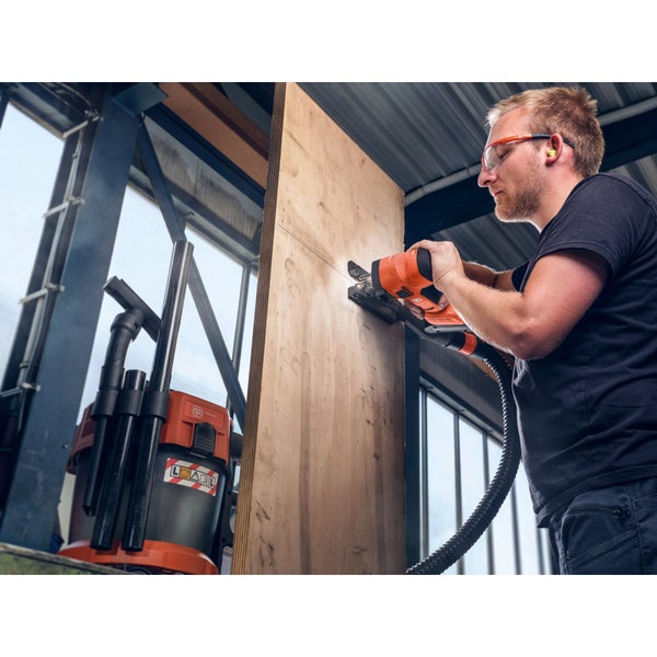 Ein Handwerker sägt mit einer Stichsäge eine Holzplatte, die an einen Baustaubsauger mit Absaugschlauch angeschlossen ist.