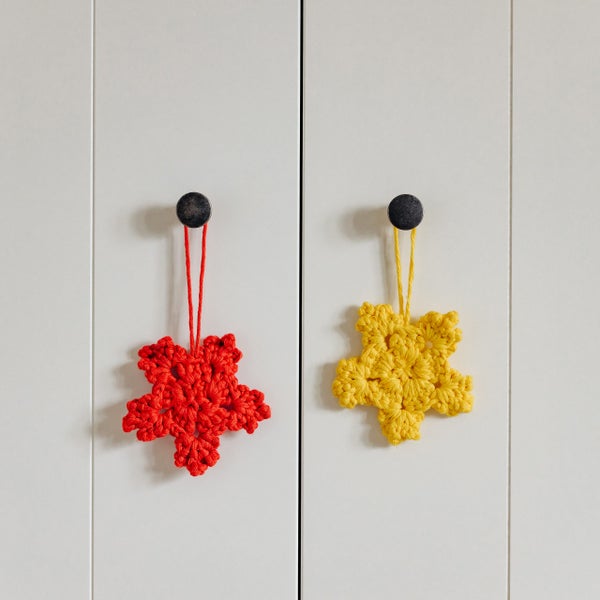 Gehäkelte rote und gelbe Sterne als Anhänger an dunklen Möbelknöpfen an einem Schrank.