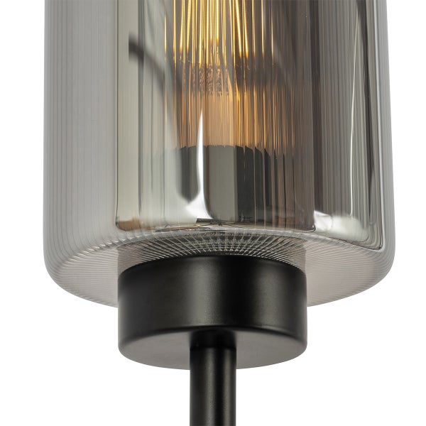 Detailansicht einer Leuchte mit geriffeltem Glasschirm aus Rauchglas und schwarzem Metallsockel mit leuchtendem Glühfaden.