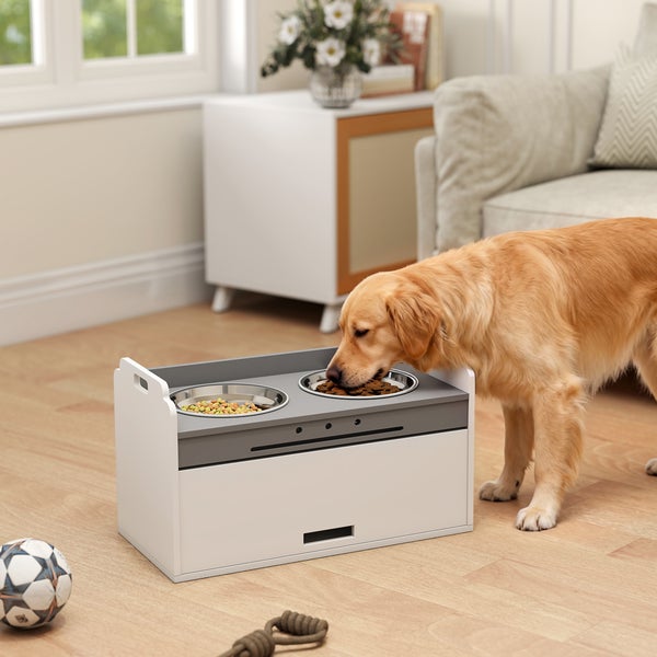 Erhöhte Futterstation aus Holz mit zwei Edelstahlnäpfen in einem hellen Wohnzimmer, an der ein Golden Retriever frisst.