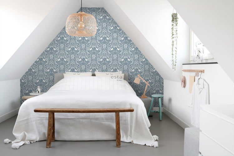 Schlafzimmer im Dachgeschoss mit gemusterter Tapete, Bett mit Tagesdecke und Holzbank