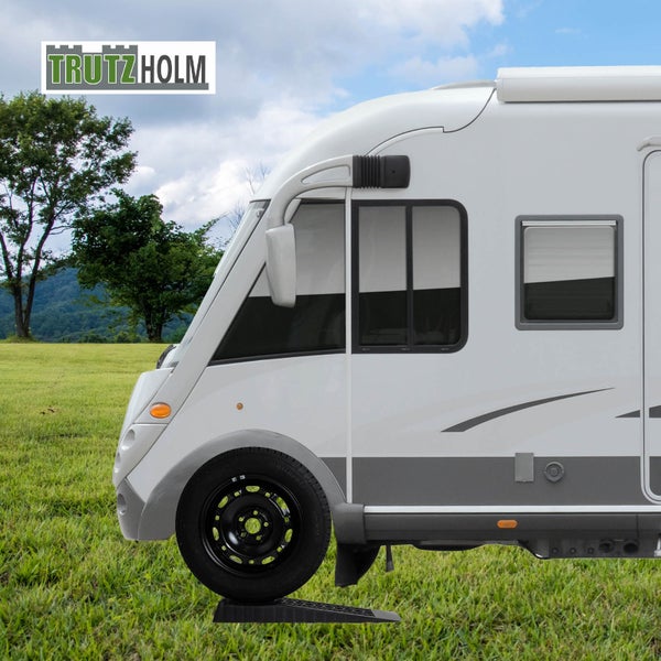 Wohnmobil steht auf einer Auffahrhilfe zur Ausrichtung auf einer Rasenfläche. TrutzHolm Logo.