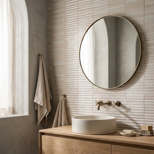 Modernes Badezimmer mit rundem Spiegel, Aufsatzwaschbecken, Holzwaschbeckenunterschrank und Wandfliesen mit strukturierter Oberfläche.