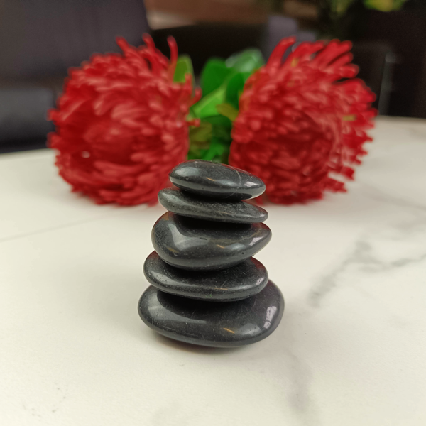 Fünf gestapelte glatte schwarze Natursteine für Wellness und Dekoration vor Blumen auf einem hellen Untergrund.