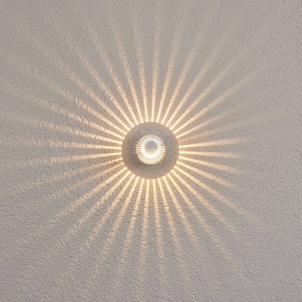 Runde LED-Wandleuchte mit strahlenförmigem Lichteffekt auf einer strukturierten Oberfläche.