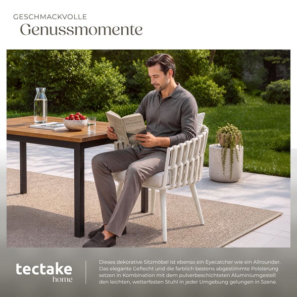 Ein Mann liest ein Buch auf einem modernen Gartenstuhl mit Geflechtoptik an einem Tisch auf einer Terrasse im Freien.