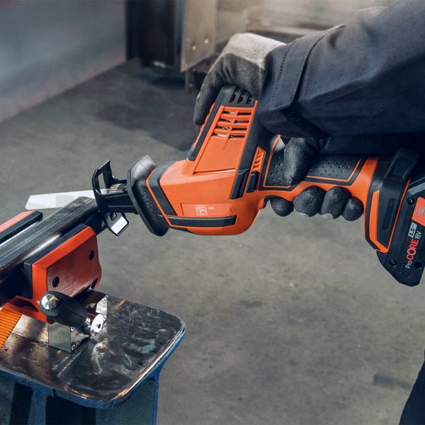 Person schneidet mit einer orangefarbenen Fein Akku-Säbelsäge ein in einem Schraubstock eingespanntes Metallprofil in einer Werkstatt.