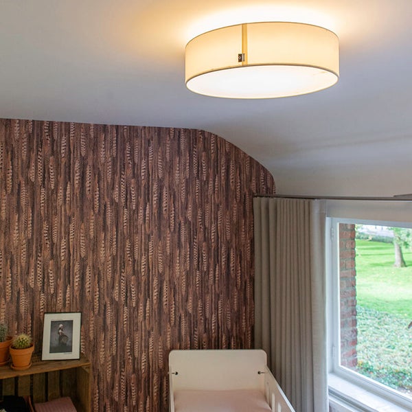 Runde Stoff-Deckenleuchte in einem hellen Kinderzimmer mit gemusterter Tapete und Kinderbett.
