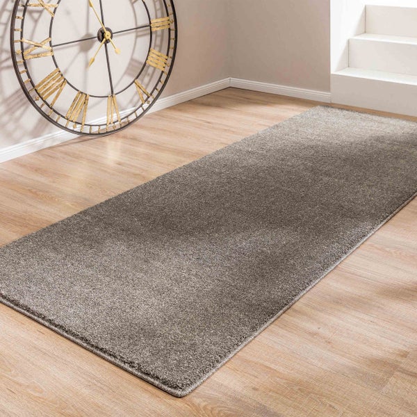 Grauer Teppichläufer auf hellem Bodenbelag in Holzoptik neben einer weißen Treppe und einer großen Wanduhr.