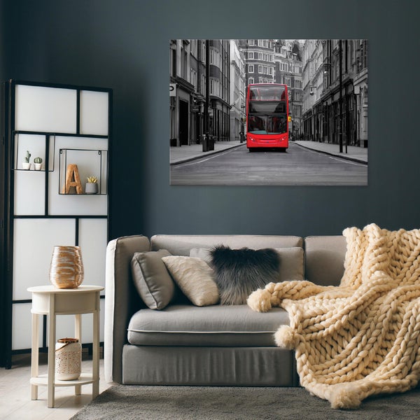 Wandbild mit Motiv eines roten Londoner Busses in einer schwarz-weißen Stadtkulisse, aufgehängt über einem Sofa in einem modernen Wohnzimmer.