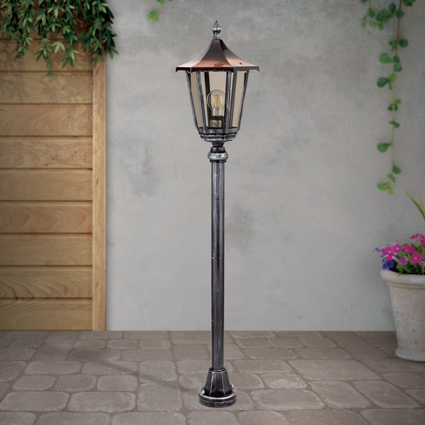 Klassische Gartenlaterne aus Metall und Glas auf einer gepflasterten Terrasse.