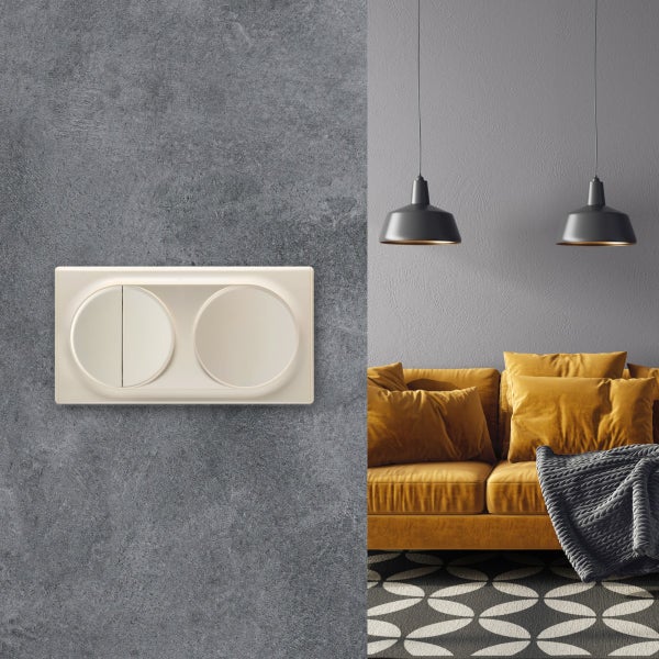 Doppelwippschalter an einer grauen Wand neben einem modernen Wohnzimmer mit Sofa und Hängeleuchten