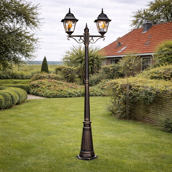 Zweiflammiger Kandelaber aus Metall im klassischen Stil auf einer Rasenfläche in einem hellen, gepflegten Garten mit Haus.