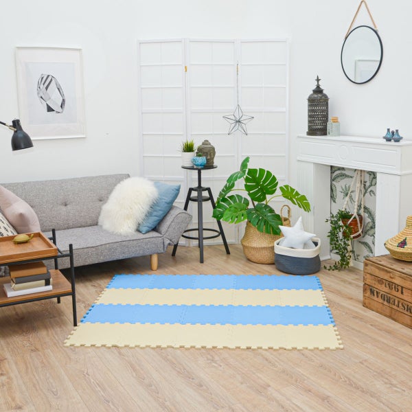 Weiche Schaumstoff-Puzzlematte mit Streifenmuster auf hellem Holzboden in einem hellen, organisierten Wohnzimmer mit grauem Sofa und Pflanzen.