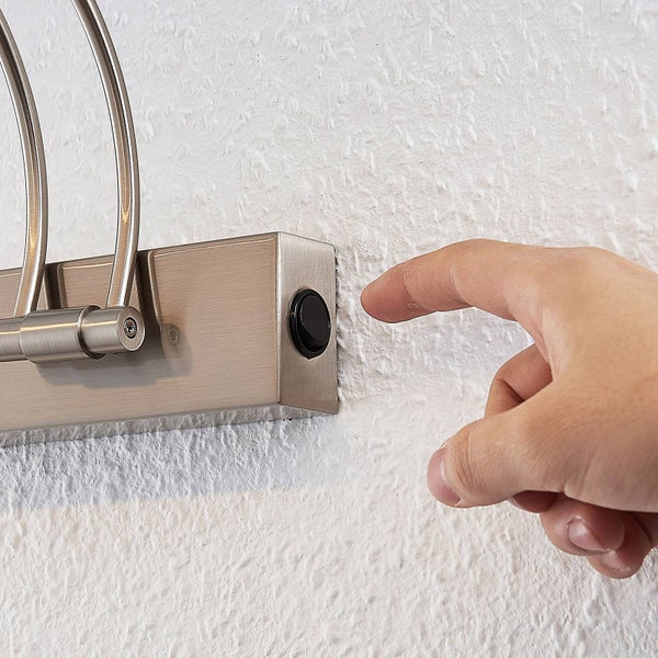 Nahaufnahme einer Hand, die den Wippschalter an einer Wandleuchte aus Metall bedient.