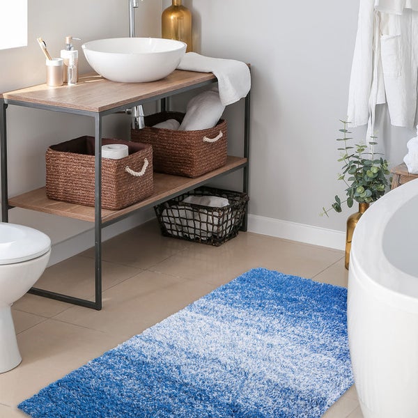 Badezimmeransicht mit blau-weißem Badteppich, Waschtisch mit Aufsatzwaschbecken und Körben