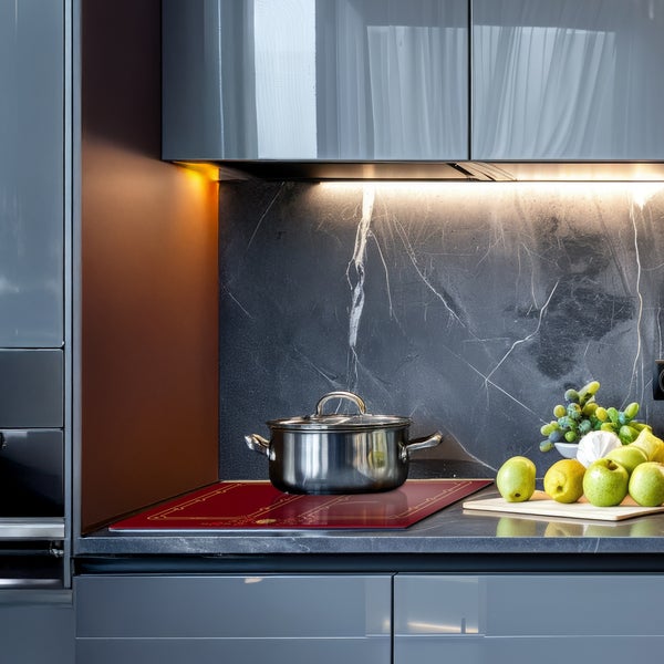 Moderne Küche mit Kochfeldabdeckung auf dem Herd und Edelstahltopf sowie frischem Obst auf der Arbeitsplatte mit dunkler Marmoroptik.