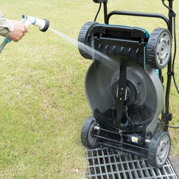 Eine Person reinigt einen Rasenmäher mit einem Wasserschlauch auf einem Rasen