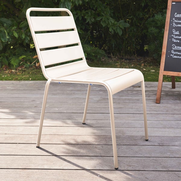 Moderner Gartenstuhl aus Metall mit Querlatten auf einer Holzterrasse, umgeben von Pflanzen und einer Menütafel in heller Umgebung.