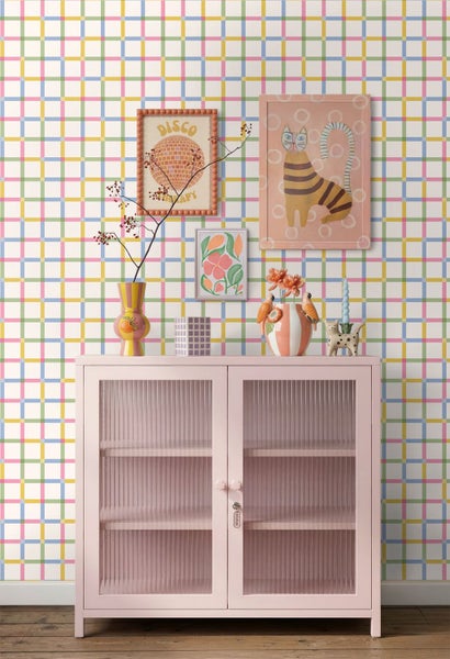 Bunte Vliestapete mit Karomuster hinter einer rosa Anrichte mit verschiedenen Dekorationsgegenständen im modernen Wohnraum.