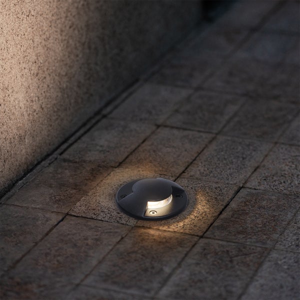 Runde schwarze Bodeneinbauleuchte auf Steinplatten installiert mit warmweißem Lichtschein.