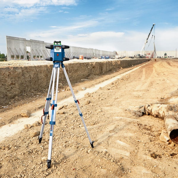 Ein Bauarbeiter mit Schutzhelm benutzt eine digitale Wasserwaage an einem Metallrahmen auf einer Baustelle.