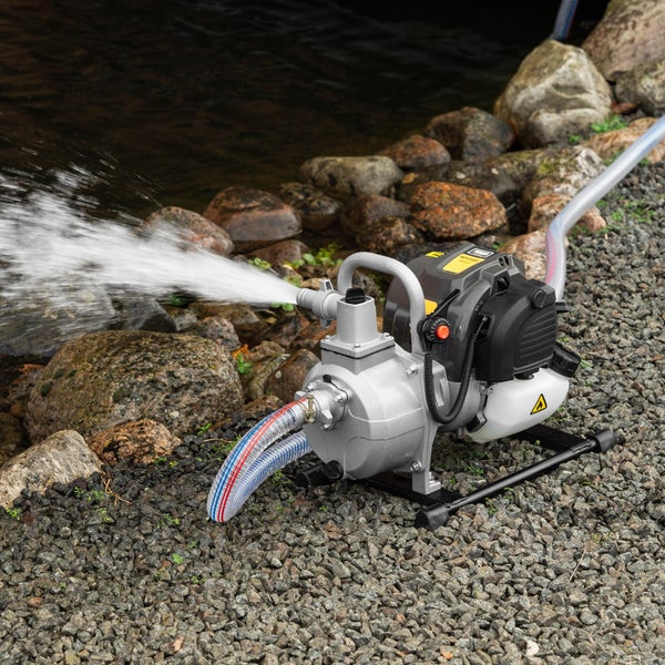 Eine benzinbetriebene Wasserpumpe pumpt Wasser aus einem Teich an einem steinigen Ufer.