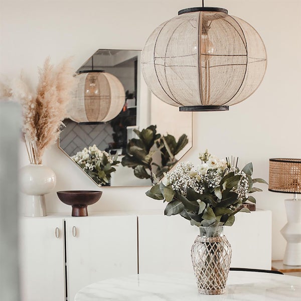 Runde Pendelleuchte mit Stoffschirm in einem hell eingerichteten Wohnzimmer mit Spiegel und Tischdekoration.