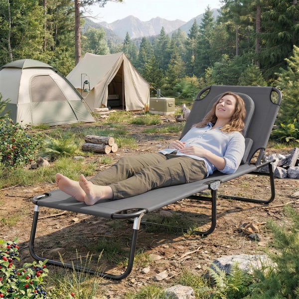 Klappbare Campingliege mit Kopfstütze in einer Berglandschaft mit Zelten im Hintergrund.