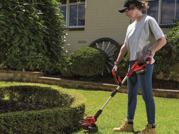 Eine Person verwendet einen Einhell Akku Rasentrimmer zur Pflege der Rasenkanten in einem sonnigen Garten.