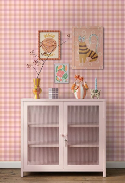 Karierte Vliestapete in Rosa und Beige an einer Wand mit einem rosa Vitrinenschrank, Vasen und verschiedenen Wandbildern.