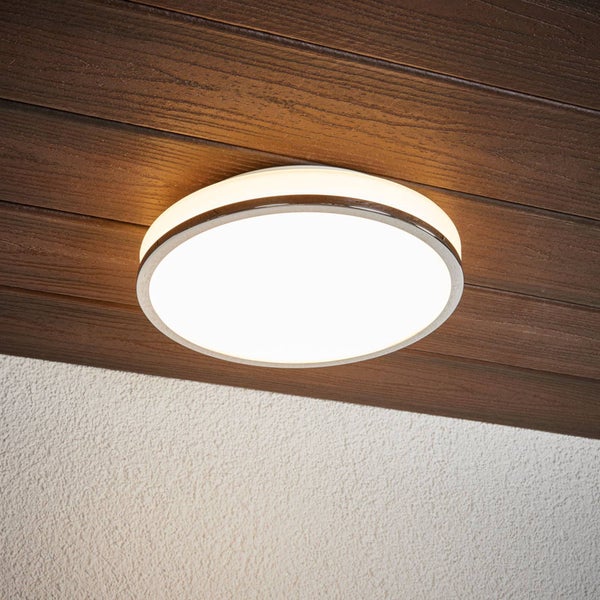 Runde LED-Deckenleuchte mit Metallrand, montiert an einer dunklen Holzdecke, beleuchtet eine weiße Wand mit Struktur.