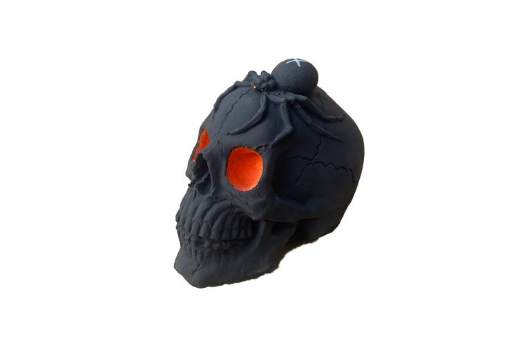 Schwarzer Totenkopf als Halloween-Dekoration mit einer Spinne auf dem Kopf und leuchtend orangefarbenen Augen.