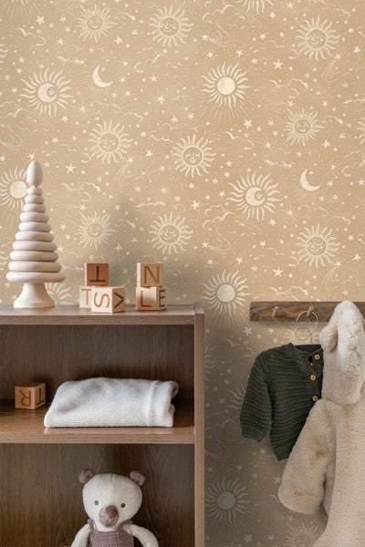 Vliestapete für Kinderzimmer mit Himmelsmotiven wie Sonnen, Monden und Sternen in beigen Farbtönen, kombiniert mit Holzspielzeug.