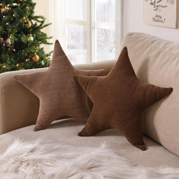 Zwei sternförmige Dekokissen mit strukturierter Oberfläche auf einem Sofa vor einem geschmückten Weihnachtsbaum.
