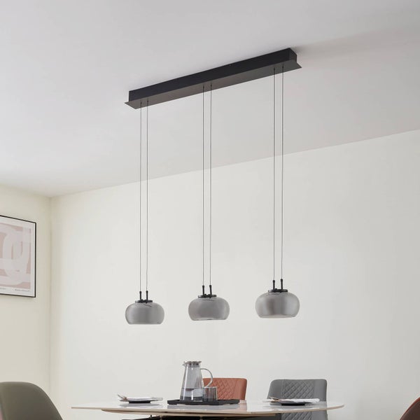 Dreiflammige Pendelleuchte mit grauen Glasschirmen und schwarzer Deckenleiste über einem Esstisch in einem hellen, modern eingerichteten Raum.
