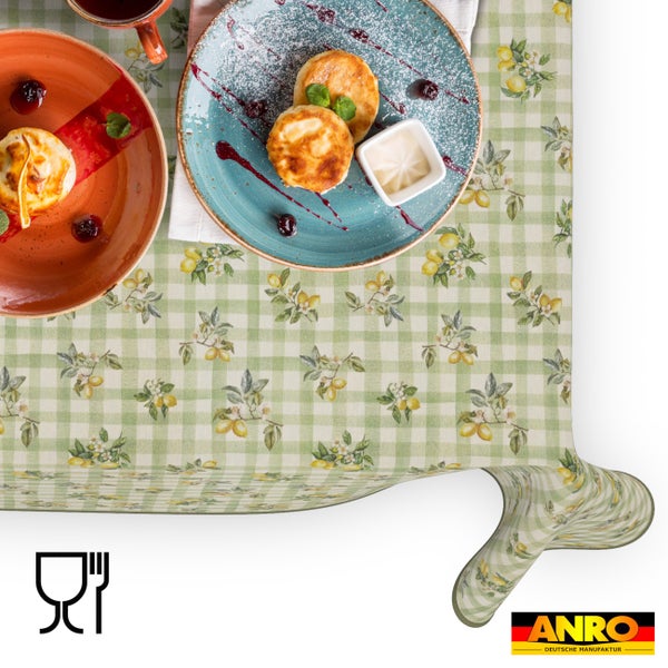Abwaschbare Wachstuch-Tischdecke mit grünem Karomuster und Zitronenmotiven, hell gedeckter Tisch mit Frühstück, lebensmittelecht, ANRO Logo.